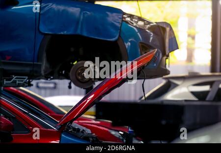 Atelier de réparation automobile. Voiture rouge capot ouvert sur fond flou de voiture SUV bleue soulevée dans le garage pour réparation et entretien. Vérification de la voiture. Banque D'Images