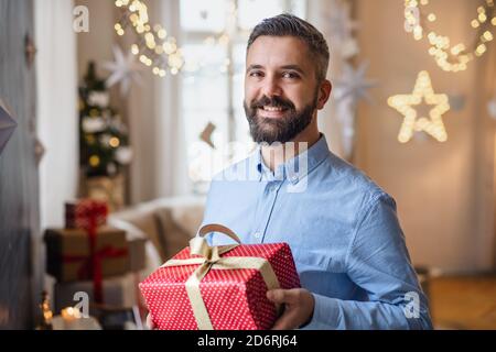 Homme mature à l'intérieur à la maison à Noël, tenant le présent. Banque D'Images