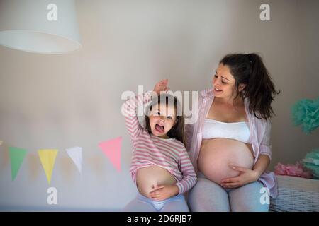 Portrait d'une femme enceinte avec une petite fille à l'intérieur à la maison, montrant le ventre. Banque D'Images