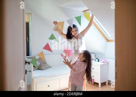 Portrait d'une femme enceinte avec une petite fille à l'intérieur à la maison, décorant la chambre. Banque D'Images