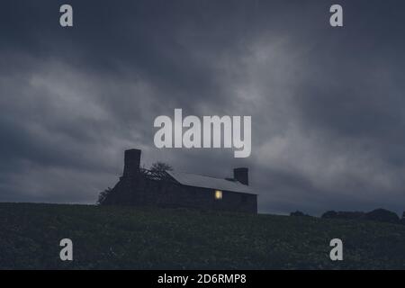 Une maison en ruines au milieu de la campagne. Avec une lumière qui brille d'une fenêtre cassée sur une nuit de tempête Banque D'Images