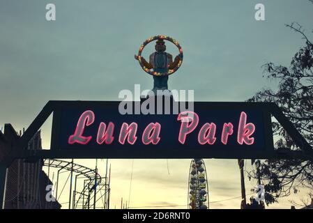 Clown illuminé et effrayant sur le panneau d'un luna Park avec une roue de ferris et d'autres jouets funky sur fond avec beau ciel crépuscule, Halloween hor Banque D'Images