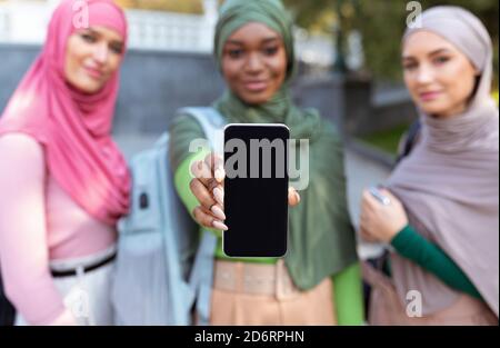 Trois femmes musulmanes montrant l'écran d'un smartphone à l'extérieur, Focus on Phone Banque D'Images