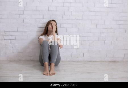 Jeune femme solitaire assise sur le sol à la maison, se sentant déprimé et désespéré, espace de copie Banque D'Images