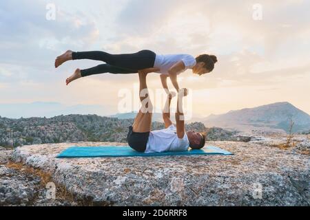 Vue latérale complète de l'homme et de la femme pratiquant le yoga acro et faisant Front Plank asana sur le sommet de la montagne rocheuse