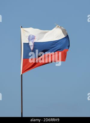 Drapeau slovène volant sur un mât sur fond bleu ciel Banque D'Images