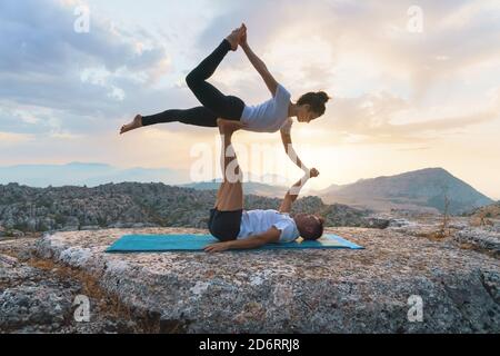 Vue latérale complète de l'homme et de la femme pratiquant le yoga acro et faisant Front Plank asana sur le sommet de la montagne rocheuse