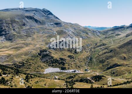 Ciel bleu clair sans nuages sur de longues allées étroites entourées par pistes de montagne couvertes d'arbres et d'herbe verdoyante Banque D'Images