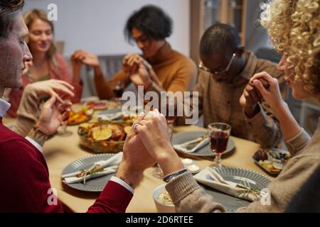 Groupe multiethnique de personnes tenant la main tout en priant au dîner de Thanksgiving avec des amis et la famille, se concentrer sur l'avant-plan, l'espace de copie Banque D'Images