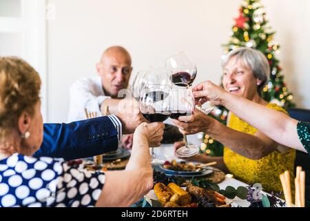 Des partenaires heureux qui élèvent des verres de boisson alcoolisée tout en se rassemblant à table pendant les fêtes dans l'appartement Banque D'Images