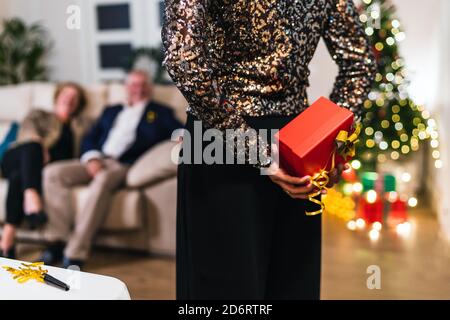 Vue arrière de la cachette de la cachette non reconnaissable Présentez-vous dans le dos tout en célébrant Noël avec vos amis à la maison Banque D'Images