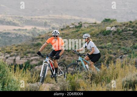 Cyclistes professionnels sérieux dans les casques et les lunettes de soleil en montant dans highlands pendant l'entraînement en été Banque D'Images