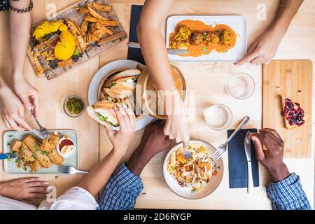 Vue de dessus crop multiethnique amis se rassembler à table dans moderne restaurant et dîner savoureux avec des boulettes de viande et sandwichs Banque D'Images