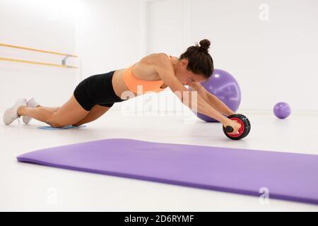 Vue latérale d'une femme élancée travaillant sur des vêtements de sport vers l'extérieur avec la roulette sur le sol, près du tapis Banque D'Images