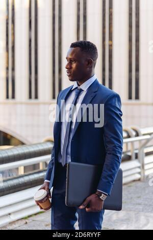 Vue latérale complète d'un homme d'affaires afro-américain respectable et confiant dans une tenue habillée marcher dans la rue contre des bâtiments contemporains dans moderne Banque D'Images