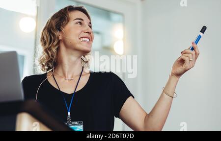 Femme d'affaires souriante pointant vers l'écran du projecteur pendant sa présentation. Femme entrepreneur donnant une présentation lors d'un séminaire. Banque D'Images