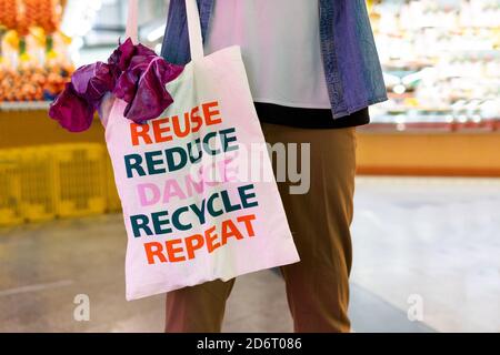 Rognez l'acheteur mâle anonyme tenant le sac de shopping en tissu avec le texte message de réutilisation et de recyclage lors des achats dans supermarché Banque D'Images