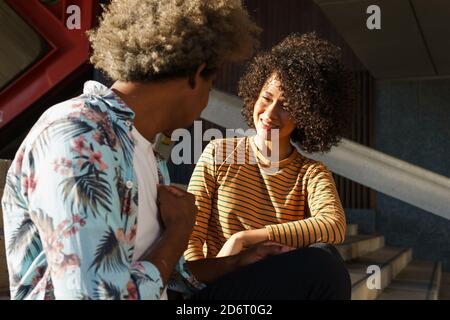 Rognez l'homme anonyme en style parlant avec le sourire ethnique Associez-vous à la coiffure afro tout en vous reposant sur l'escalier et en regardant l'un à l'autre Banque D'Images