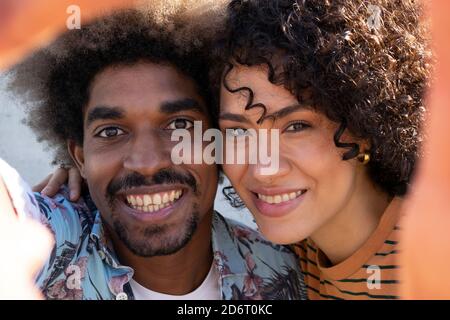 Jeune homme et femme noir joyeux avec une coiffure africaine en cuddling et regardant l'appareil photo le jour ensoleillé Banque D'Images