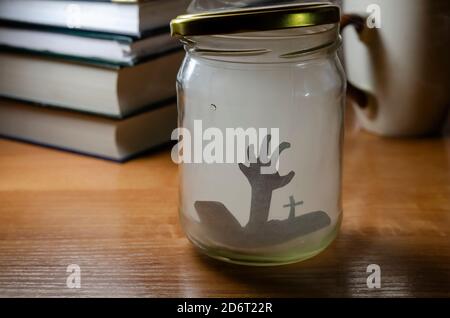 Composition de table sur le thème de l'halloween. Un pot en verre rempli de fumée avec une silhouette de main sur le fond des livres. Prise de vue à un niveau d'œil Banque D'Images