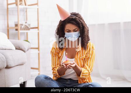 Femme noire malheureuse dans un chapeau de fête célébrant seul l'anniversaire Banque D'Images