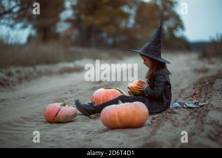 Une jolie fille en costume d'Halloween est assise sur la route dans le parc et regarde le ciel. Banque D'Images
