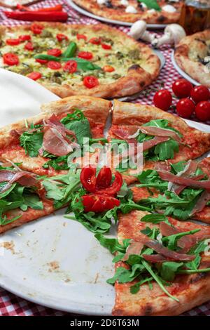 Pizza italienne en tranches appétissante au jambon de Parme et au ruccola frais servi sur table avec différents types de pizza Banque D'Images