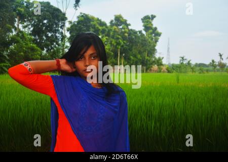 Gros plan d'une adolescente portant salwar kameez et la dhupatta bleue de la main droite sur son cou, debout sur un champ de riz, focalisation sélective Banque D'Images