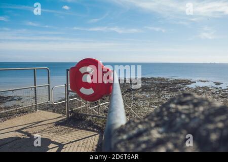 Armoire de bouée de sauvetage rouge sur une jetée vieillie contre un ciel bleu sans fin Pendant la marée basse le jour ensoleillé dans Seven Sisters Banque D'Images