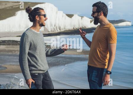 Vue latérale de jeunes hommes gais dans une ambiance décontractée vêtements et lunettes de soleil s'amuser sur la plage près de la craie Falaise dans sept Sœurs Banque D'Images