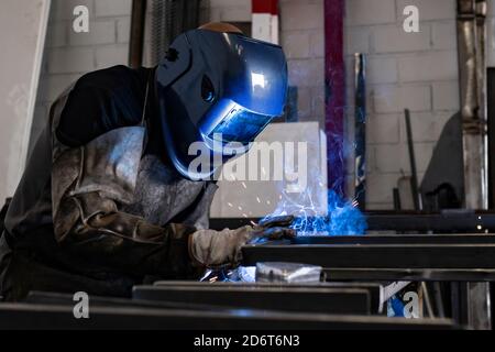 Employé masculin méconnaissable dans des gants de protection et un casque par soudage machine lors de travaux dans un atelier sombre Banque D'Images