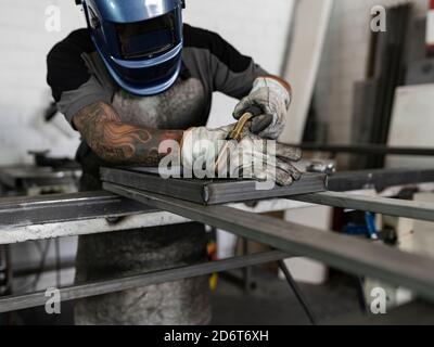 Homme méconnaissable en gants de protection et en métal de soudeur de casque avec la machine en étant debout à l'atelier Banque D'Images