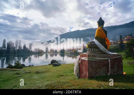 Statue de Bouddha placée près du paisible lac de Cuoka situé dans Vallée verte avec hautes montagnes et temple bouddhiste tibétain Banque D'Images