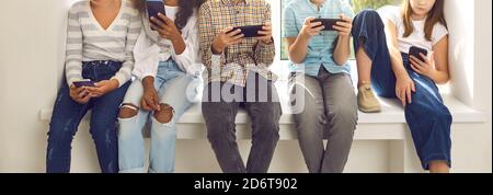 Enfants assis sur le rebord de la fenêtre et ignorant la vie réelle immergé dans leurs téléphones cellulaires Banque D'Images