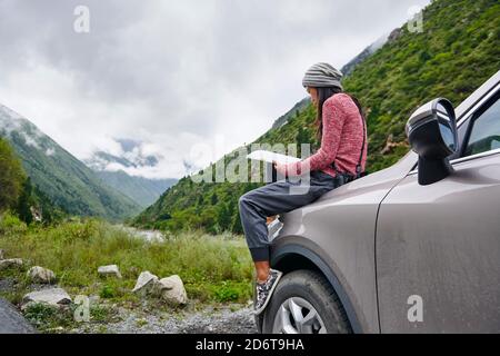 Vue latérale de la jeune femme asiatique attentionnés dans les vêtements de sport de repos en voiture avec livre dans la vallée verdoyante Banque D'Images
