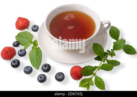 Une tasse de thé noir sur une soucoupe avec des feuilles de menthe, des fraises et des bleuets sur un fond blanc isolé. Banque D'Images