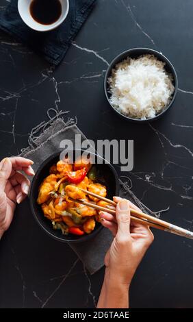 D'en haut de la récolte, une femme méconnaissable mangeant un plat de poulet asiatique et du riz avec des baguettes dans un restaurant élégant Banque D'Images