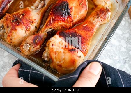 Femme main avec une serviette noire plat de service en verre avec des pattes de poulet rôties. Banque D'Images