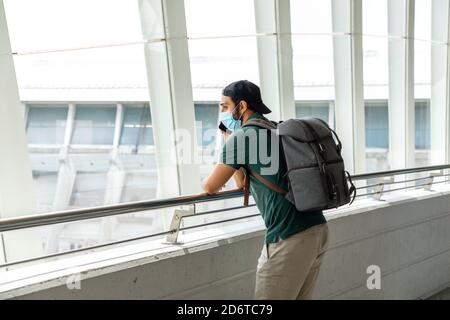 Vue latérale du voyageur de sexe masculin dans un masque médical Salon de départ de l'aéroport et en attente de vol pendant COVID 19 épidémie Banque D'Images