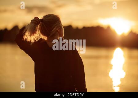 Une jeune femme regarde le soleil couchant près de la rivière. Banque D'Images