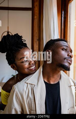 Jeune femme afro-américaine gaie en lunettes transparentes avec bouquet je regarde un homme attentionné près de la fenêtre Banque D'Images