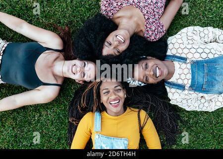Vue de dessus de enchantés amis multiraciaux se détendant sur le vert pelouse dans le parc et regarder la caméra tout en appréciant le week-end ensemble Banque D'Images