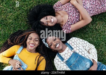Vue de dessus de enchantés amis multiraciaux se détendant sur le vert pelouse dans le parc et regarder la caméra tout en appréciant le week-end ensemble Banque D'Images