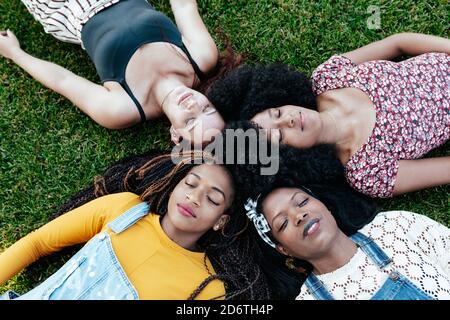 Vue de dessus de enchantés amis multiraciaux se détendant sur le vert pelouse dans le parc et les yeux fermés tout en appréciant le week-end ensemble Banque D'Images