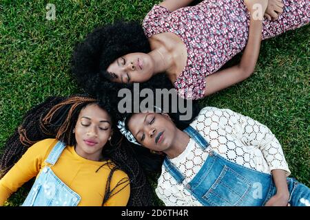 Vue de dessus de enchantés amis multiraciaux se détendant sur le vert pelouse dans le parc et les yeux fermés tout en appréciant le week-end ensemble Banque D'Images
