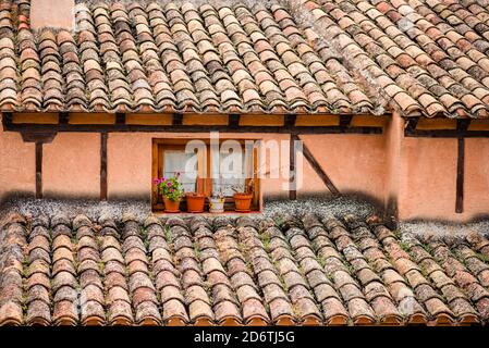 Extérieur d'un bâtiment en pierre avec carreaux de terre cuite altérés toit et fleurs en pot près d'une petite fenêtre sur la rue de Ville de Cuenca en Espagne Banque D'Images