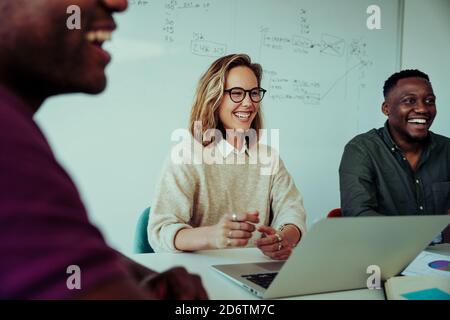 Femme d'affaires riant aux idées pour le nouveau projet présenté par des collègues assis autour de la table pendant la conférence Banque D'Images