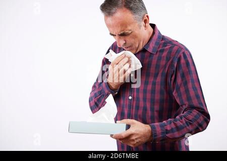 Studio Shot de l'homme mature avec le virus du rhume ou de la grippe Éternuer dans un papier de soie Agaisnt fond blanc Banque D'Images
