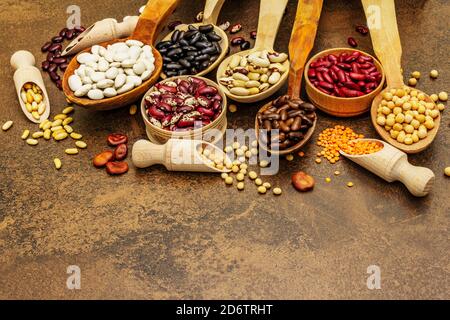 Ensemble de diverses légumineuses sèches en cuillères en bois, protéine indispensable pour un mode de vie sain. Assortiment de différents types de haricots. Cuisson en béton de pierre Banque D'Images