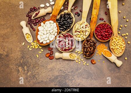 Ensemble de diverses légumineuses sèches en cuillères en bois, protéine indispensable pour un mode de vie sain. Assortiment de différents types de haricots. Cuisson en béton de pierre Banque D'Images